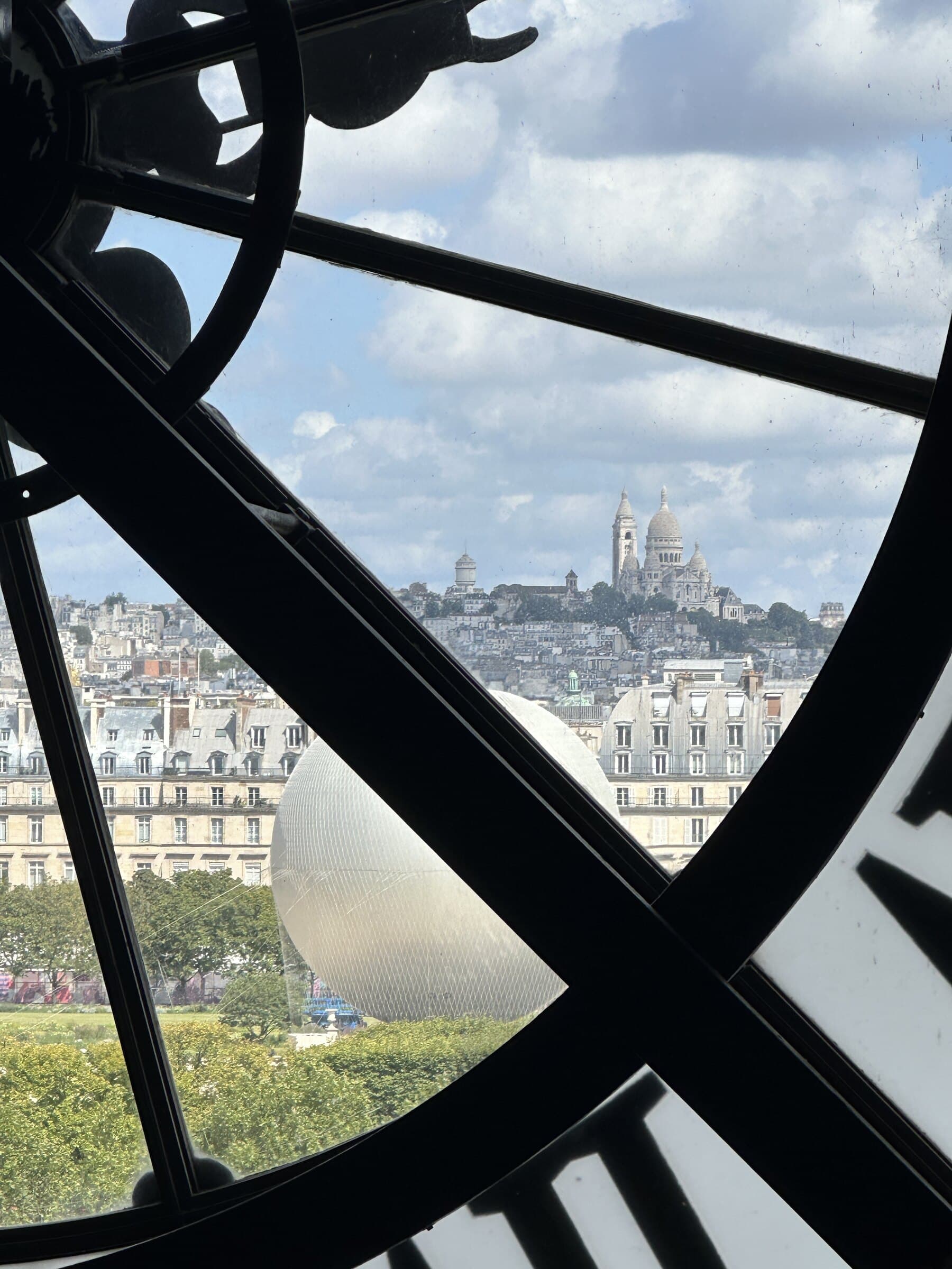 Paris clock window framing Sacré-Cœur in the distance.