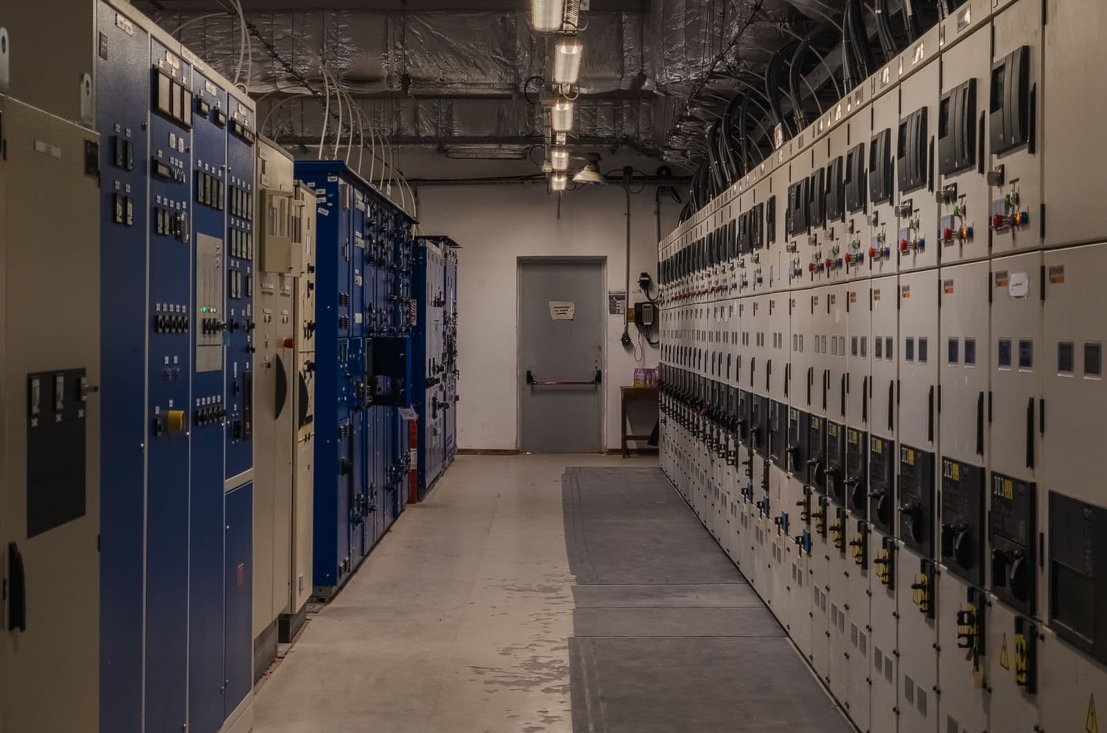 Grid control room corridor lined with electrical switchgear panels.