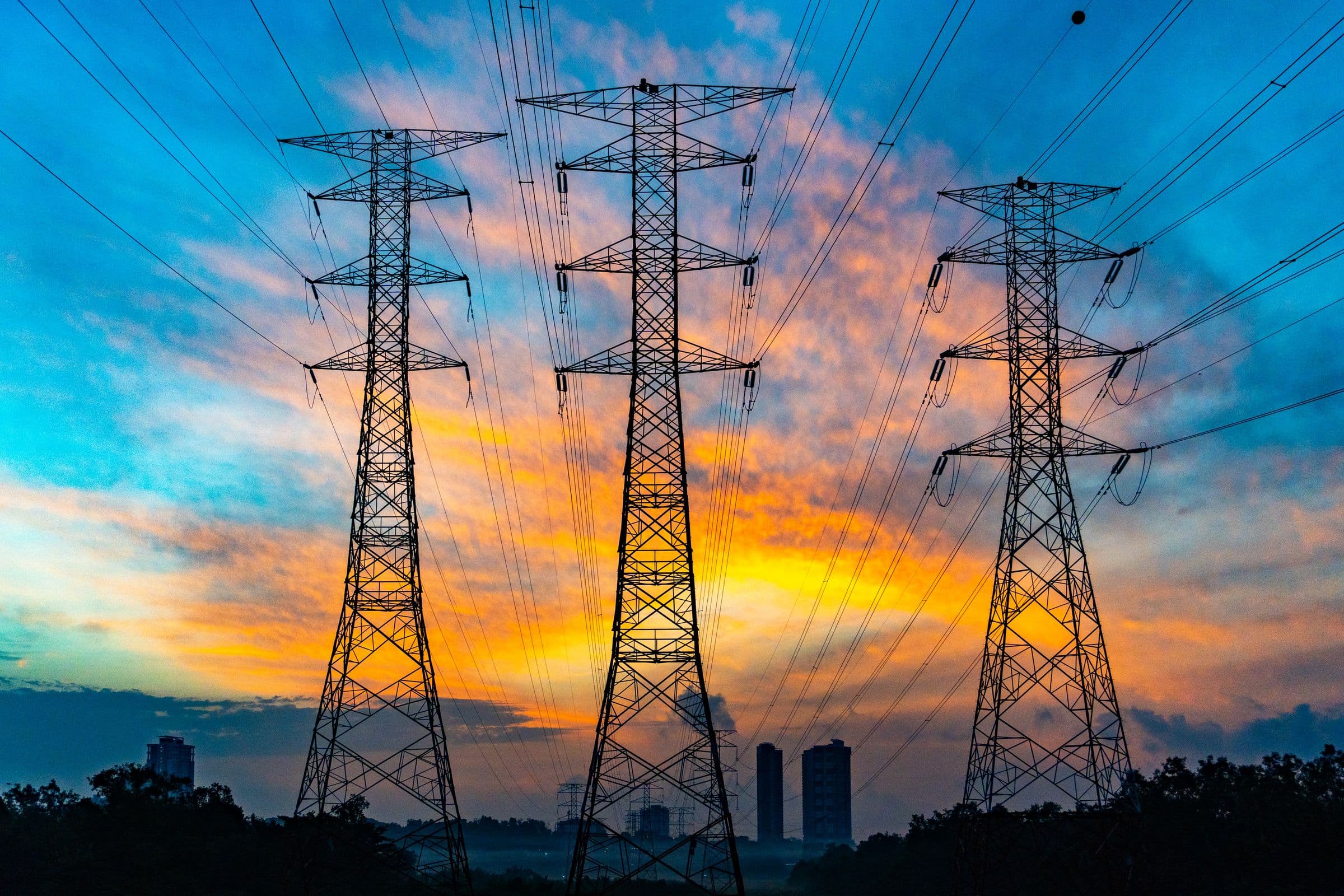 High-voltage transmission towers silhouetted against a vivid sunset sky.